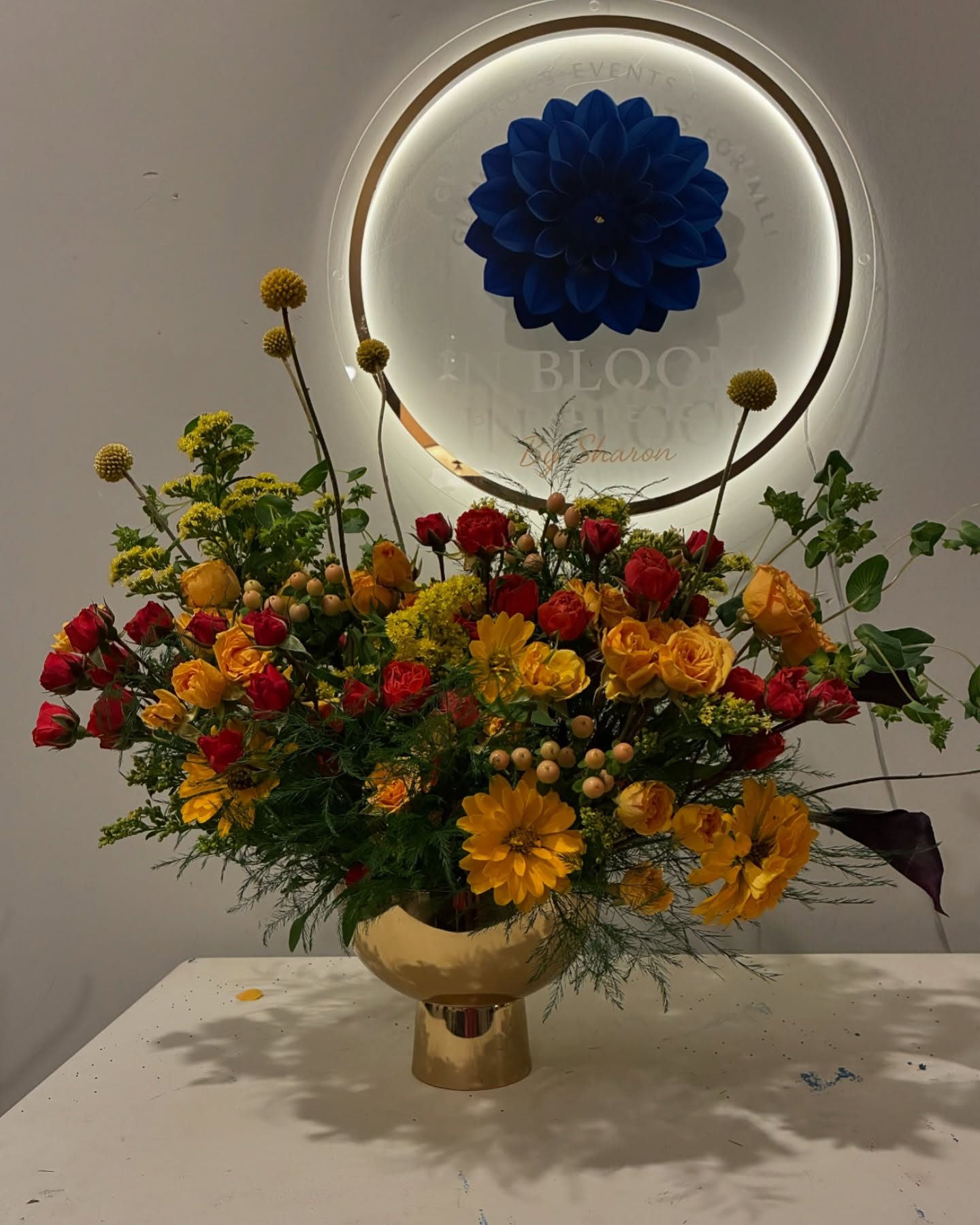 Signature arrangement of red and gold roses, dahlias, and craspedia in a gold compote at the Sharon Poindexter studio