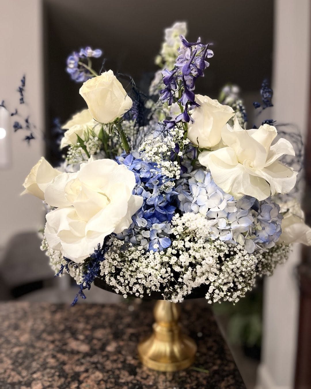 Compote arrangement of white roses, blue hydrangea, delphinium, and baby's breath