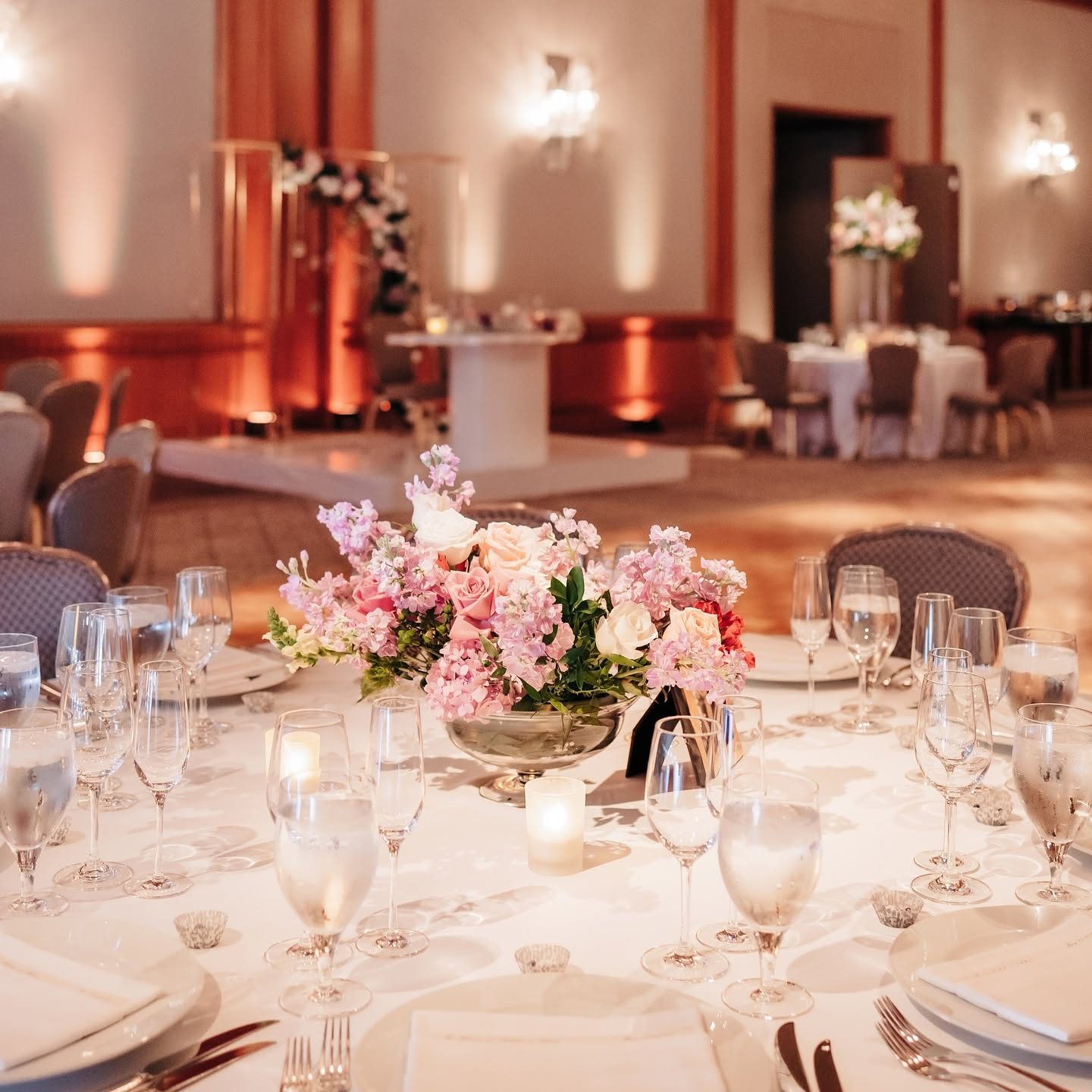 Blush pink centerpiece of roses, stock, and hydrangea in a silver compote in a ballroom
